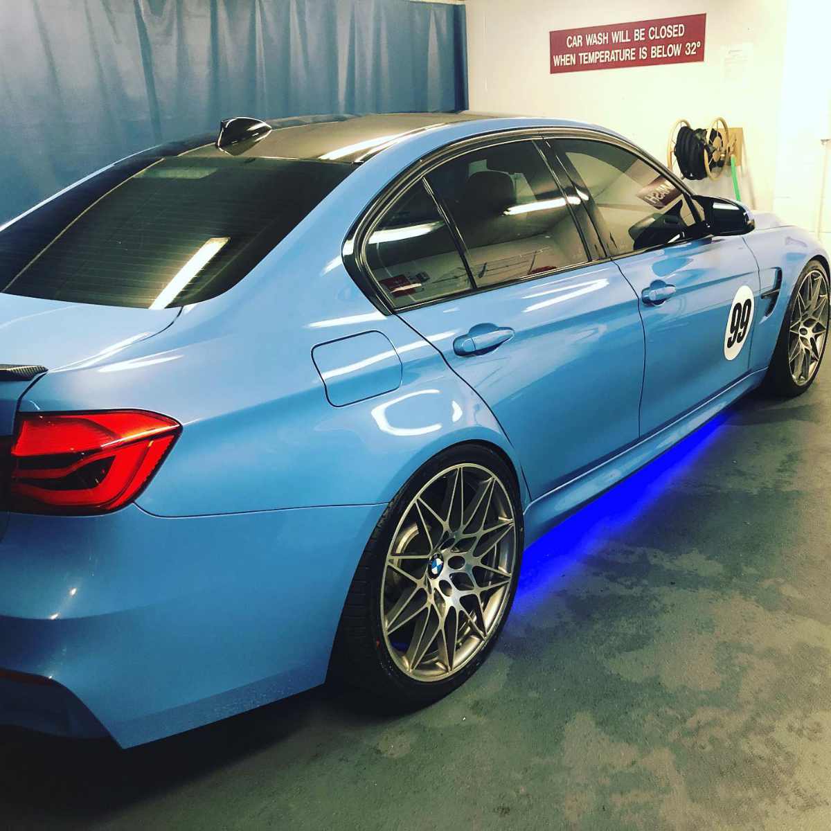 clean blue BMW with under-lighting in a wash bay