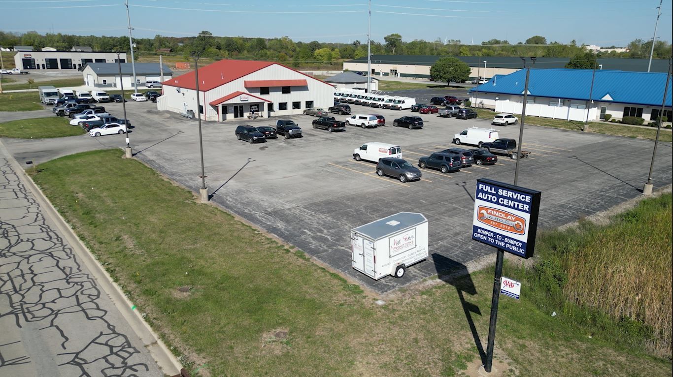 An aerial view of a commercial building and parking lot with various vehicles parked. | Findlay Auto Plus