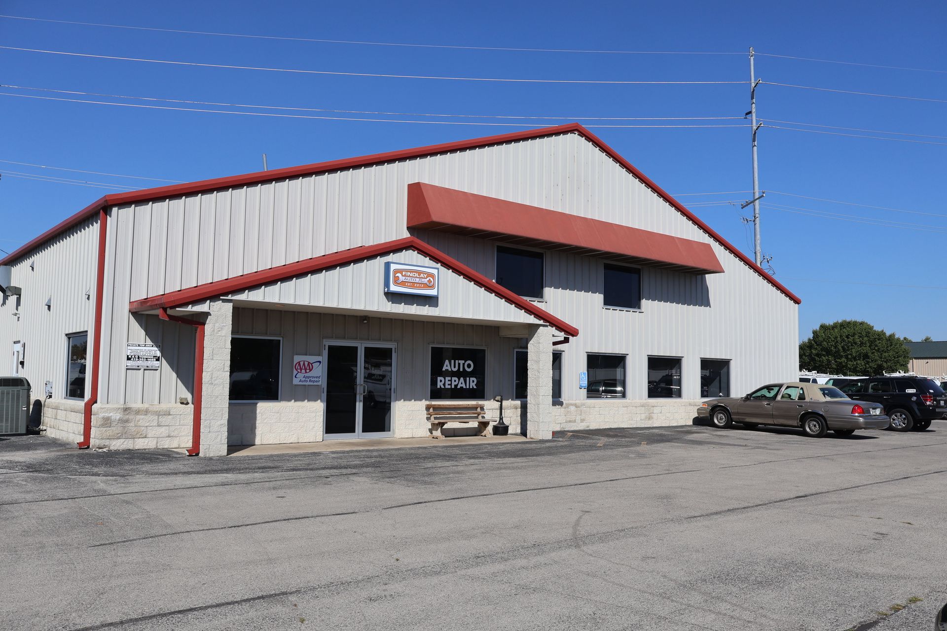 Auto repair shop building with red awning and trim, windows, and parked cars. | Findlay Auto Plus