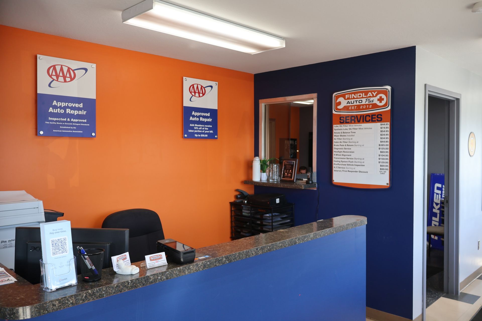 Interior of an auto repair shop's reception area. Blue and orange walls, reception counter, AAA signage, door. | Findlay Auto Plus