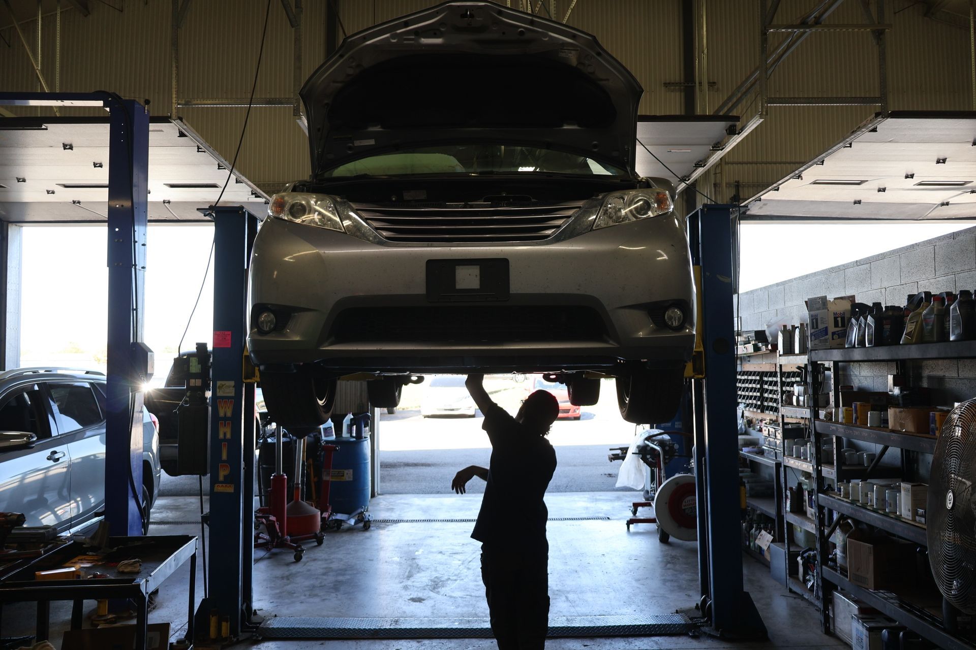 Car raised on a lift in a repair shop as a mechanic works underneath. | Findlay Auto Plus