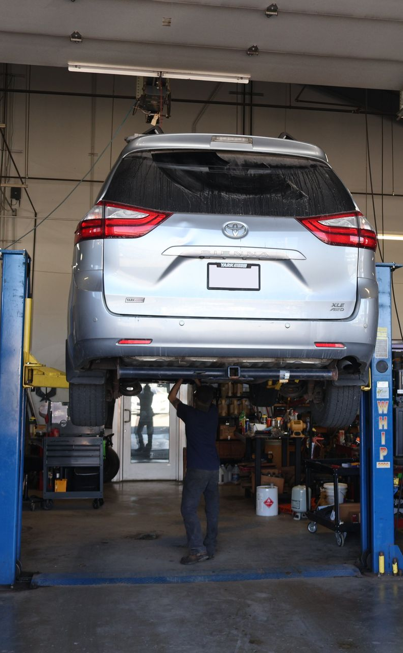 Silver SUV raised on a lift in a repair shop, mechanic working underneath. | Findlay Auto Plus