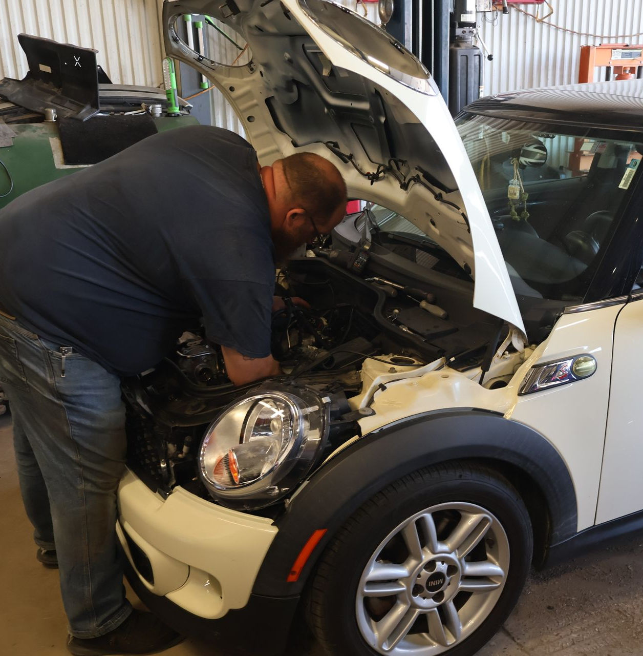 Mechanic working on a white Mini Cooper with the hood open in a garage. | Findlay Auto Plus