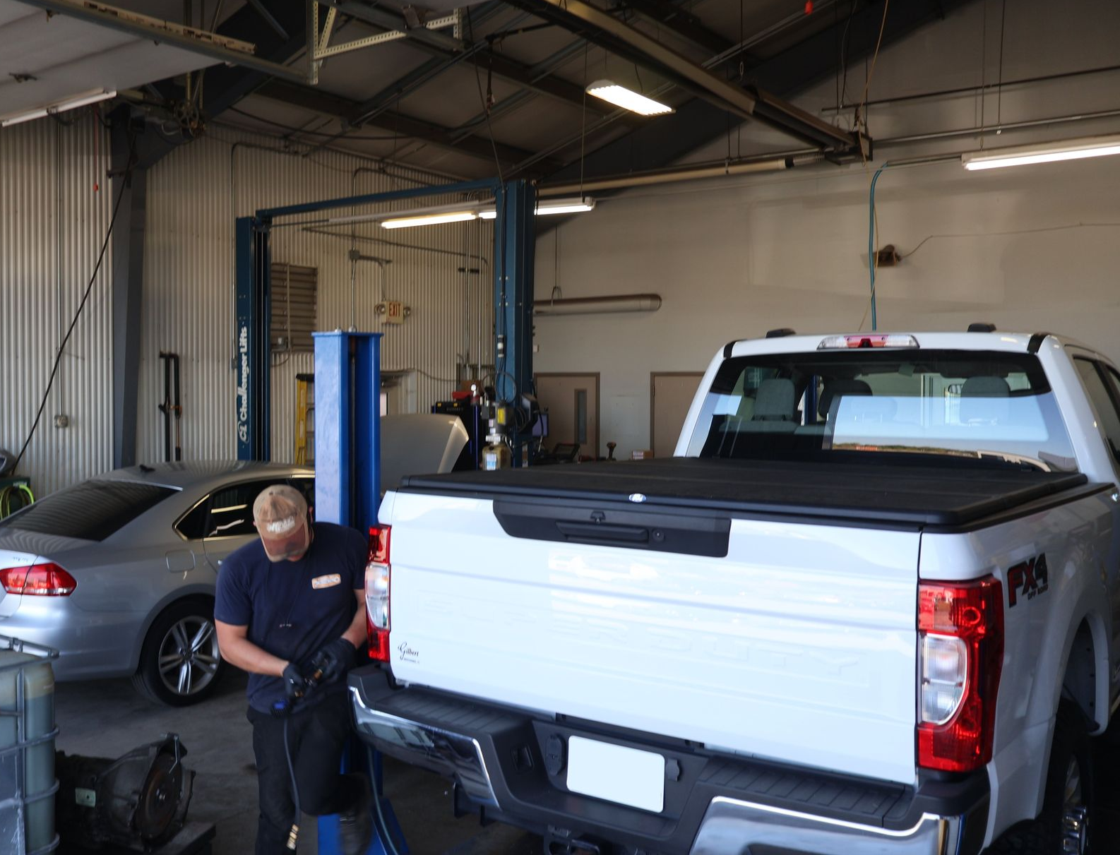 Mechanic working on the back of a white pickup truck inside an auto repair shop. | Findlay Auto Plus