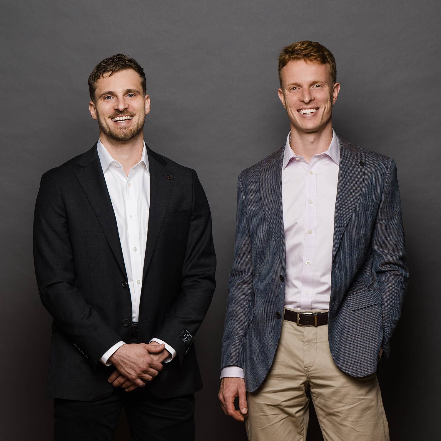 Two men in business attire, one in a black suit, one in a blue blazer