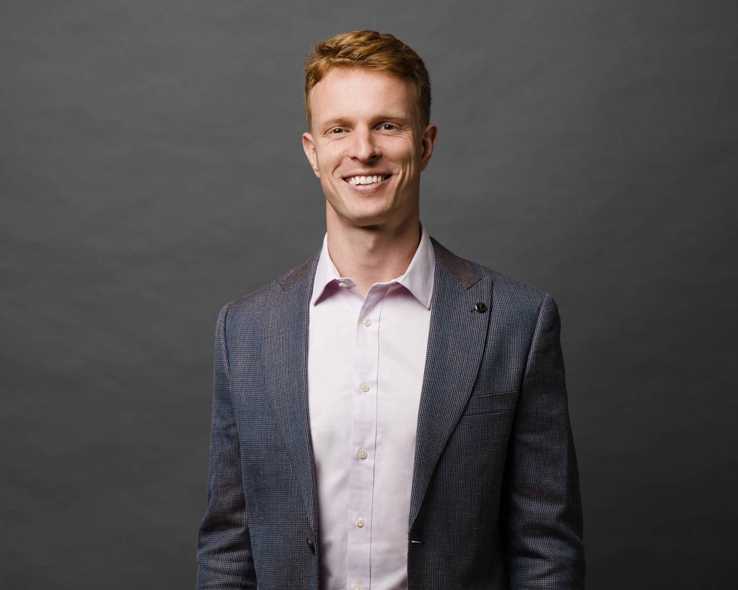 Man with red hair wearing a blazer and pink shirt