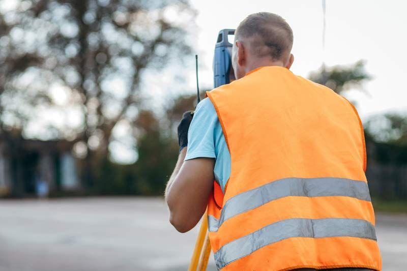 Person in orange safety vest using surveying equipment outdoors