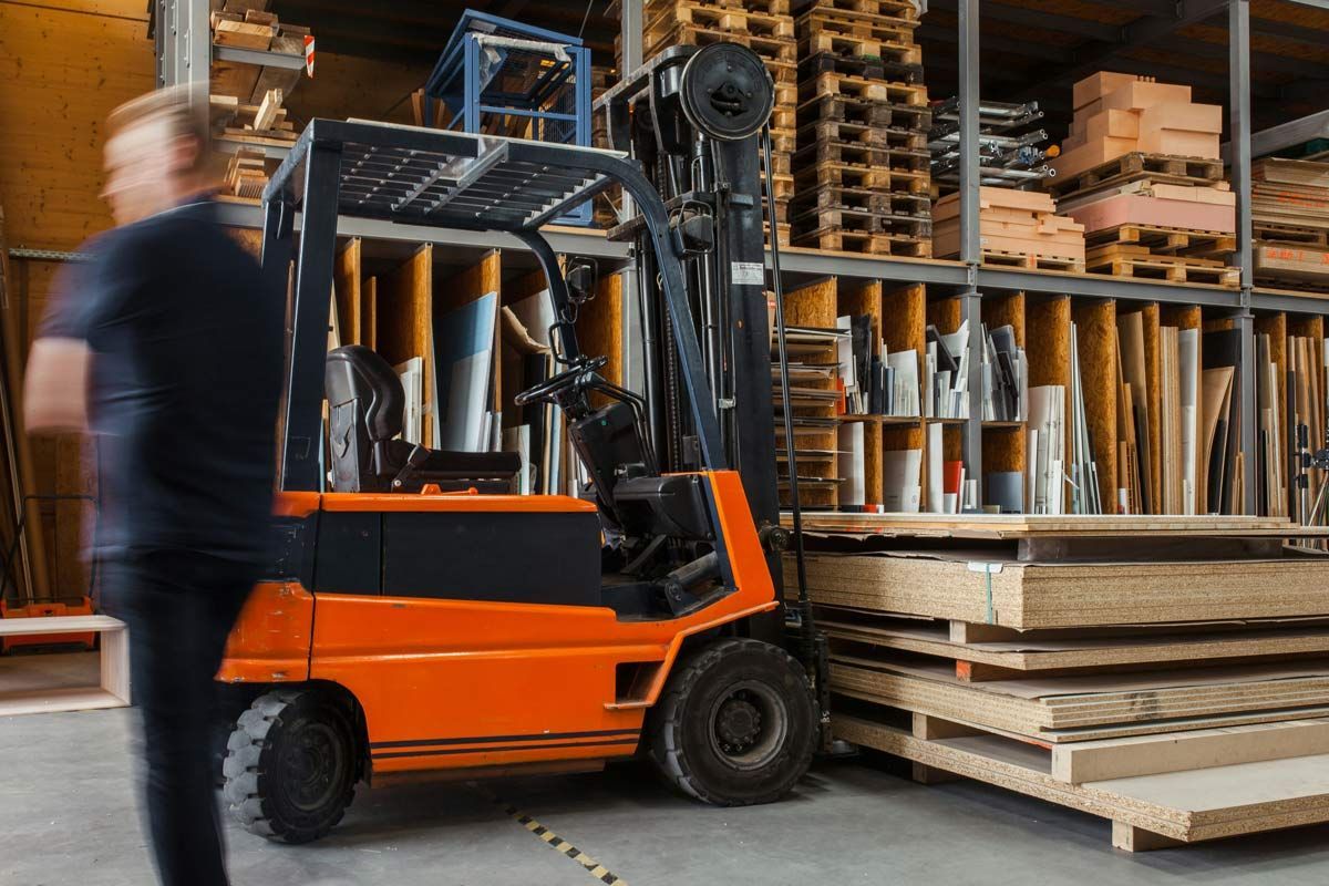 Orange forklift in warehouse, near stacks of wood