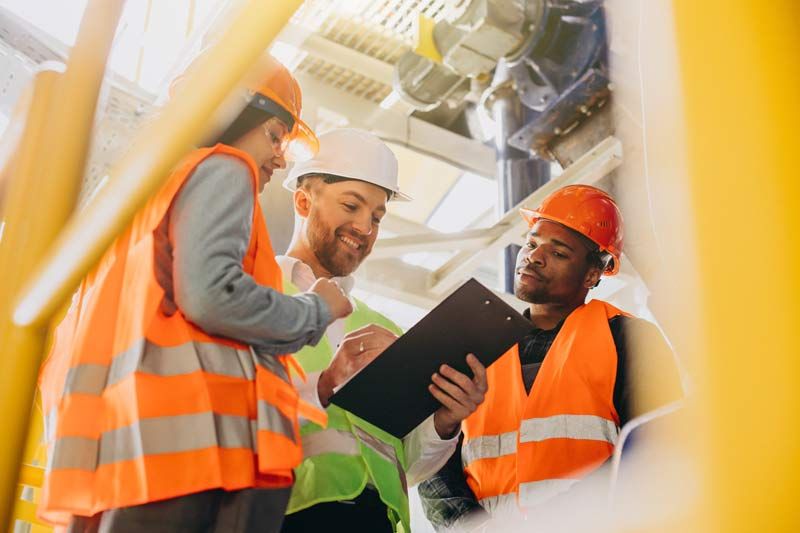 Three workers in safety vests and helmets review a clipboard