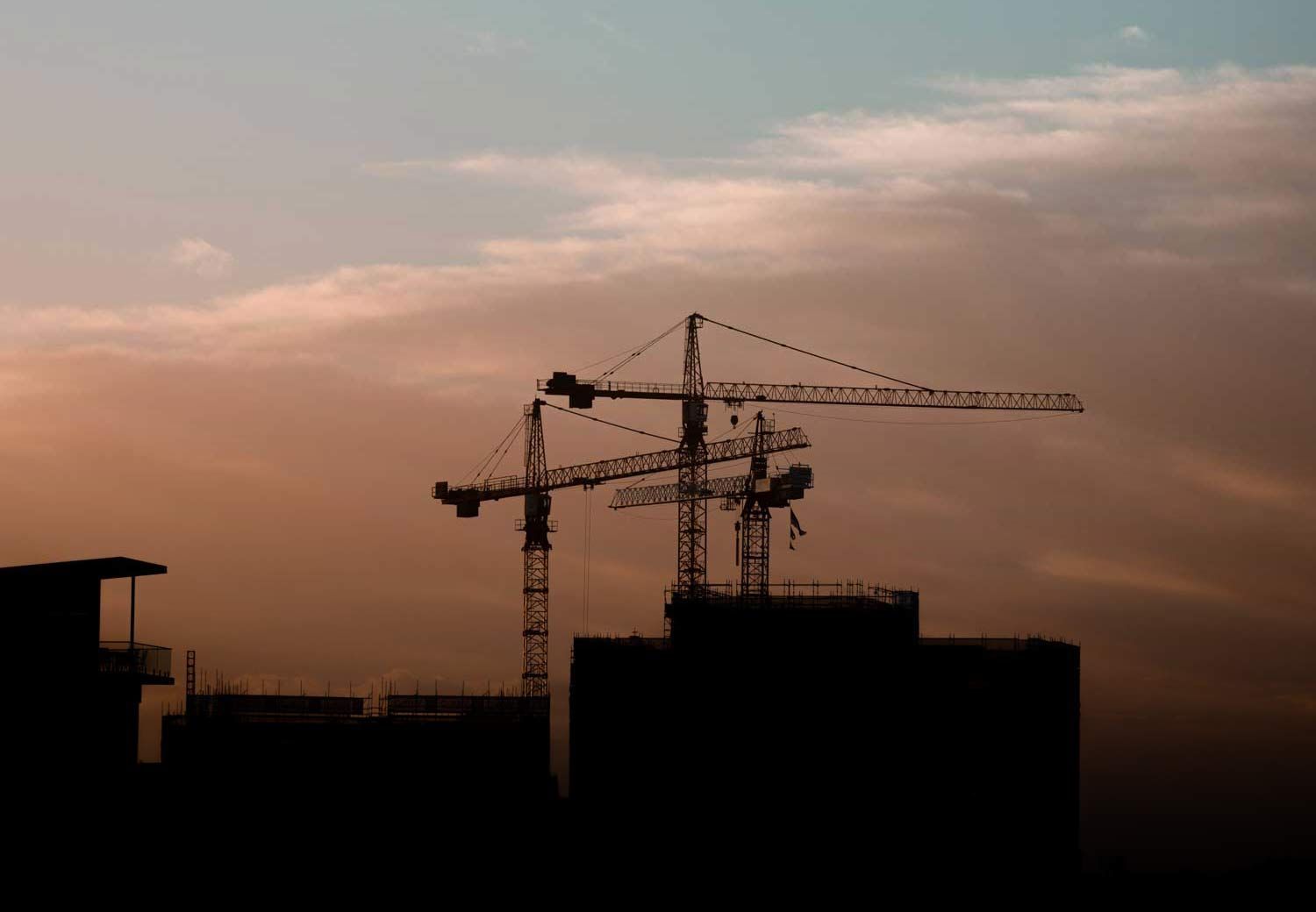 Silhouetted construction cranes atop buildings