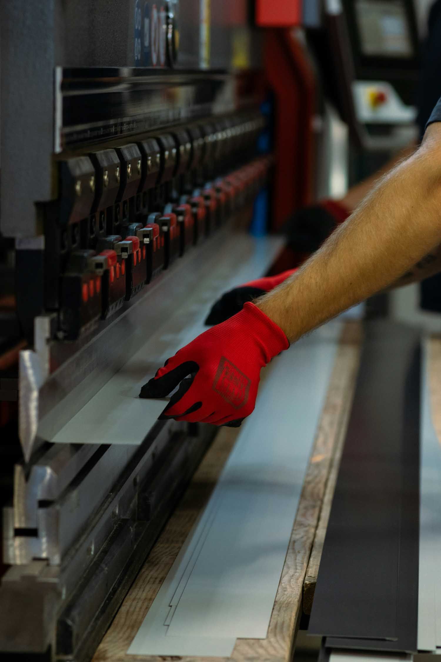 Person in red gloves bending metal sheet with industrial machine