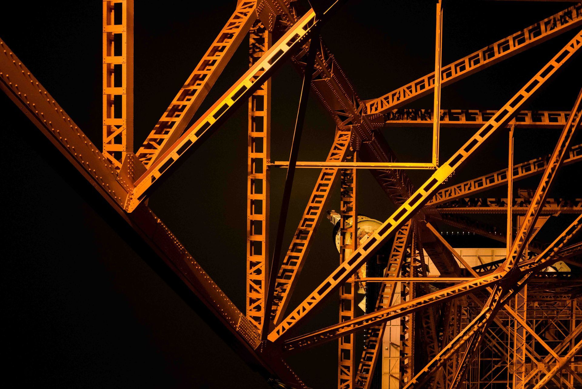 Orange-lit metal bridge structure, intricate patterns of beams and supports