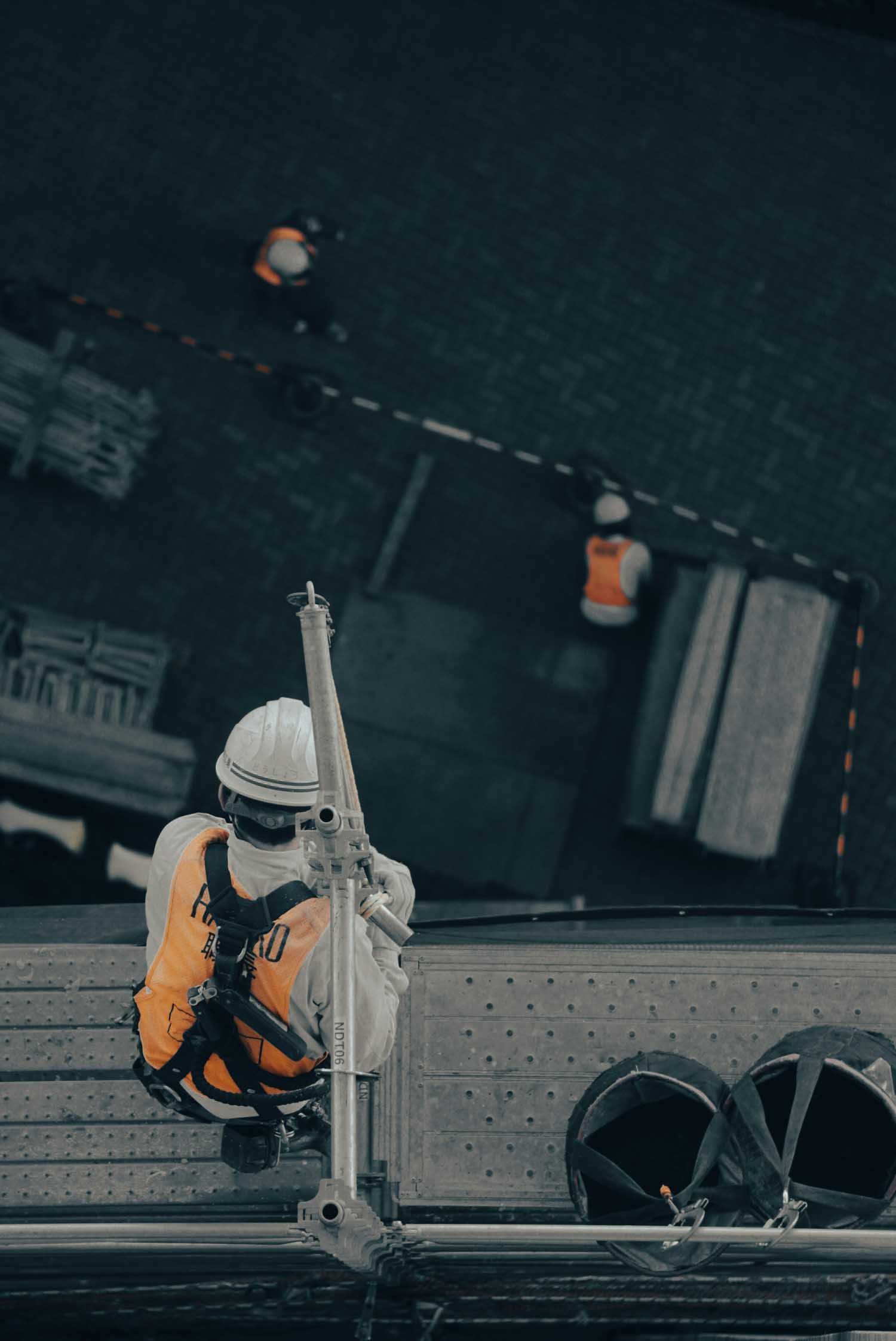 Construction worker on scaffolding, holding equipment, with others working below