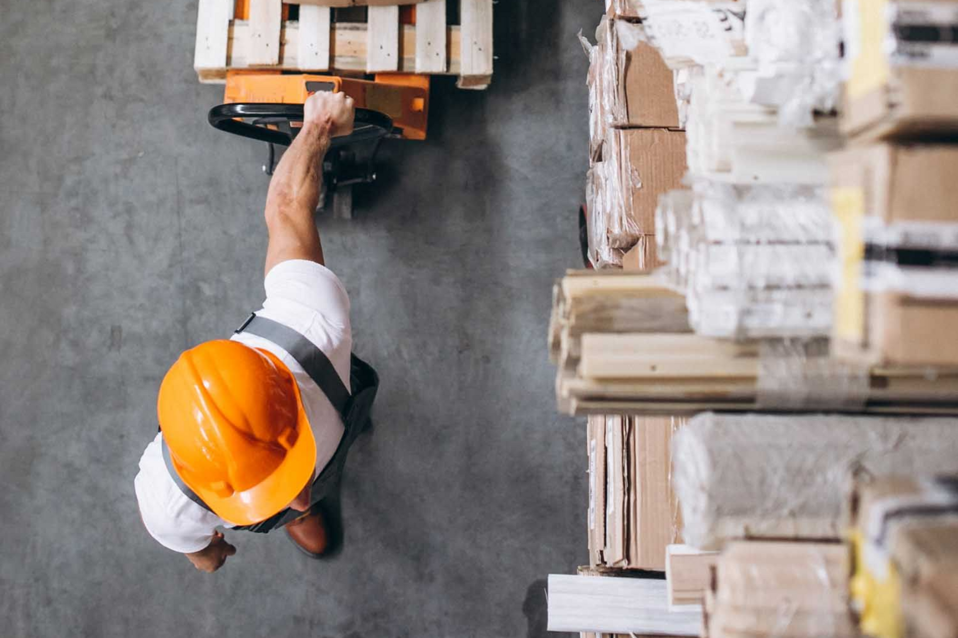 Worker in orange hard hat operating a pallet jack in a warehouse
