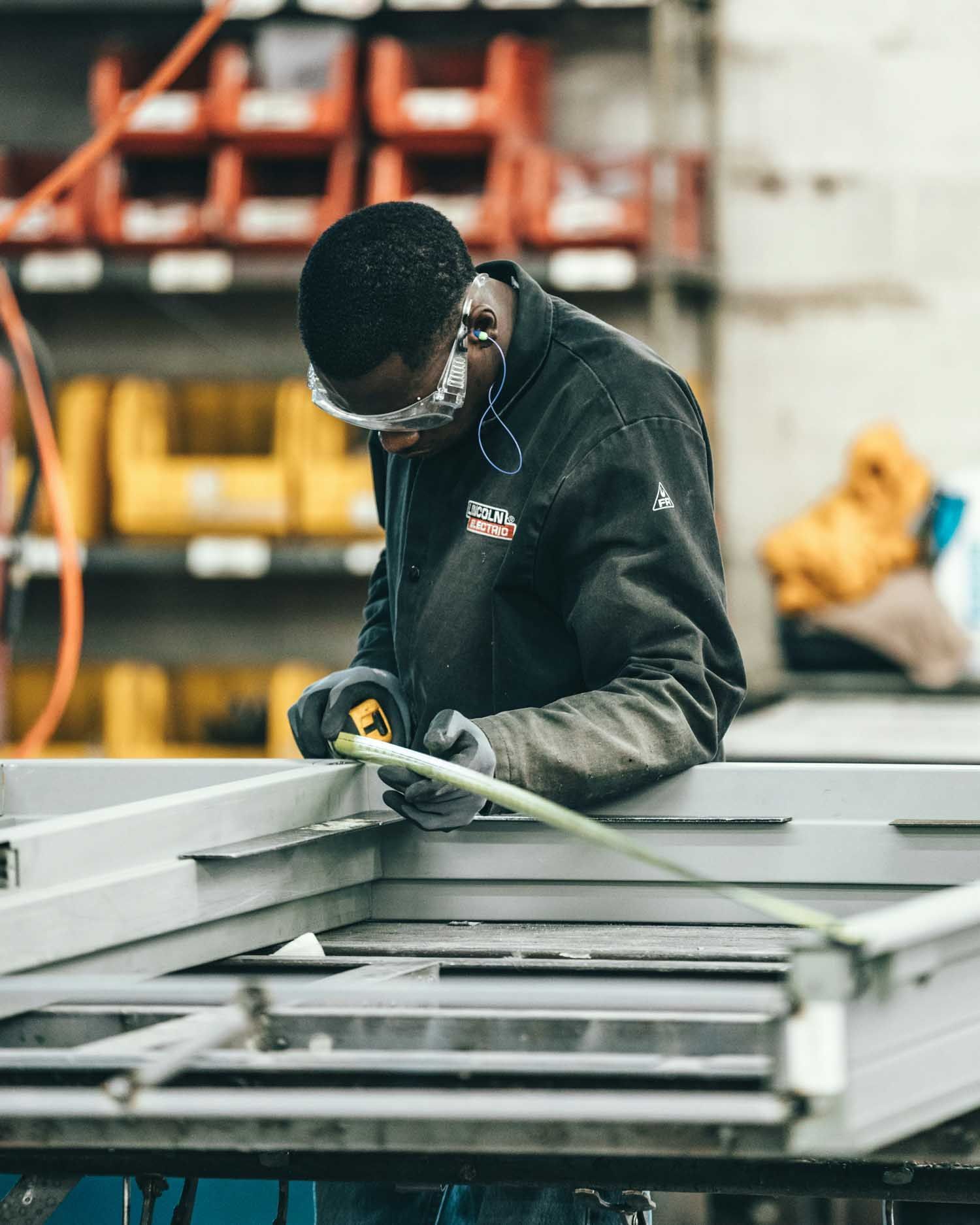 Person wearing safety glasses measuring metal frame in a workshop