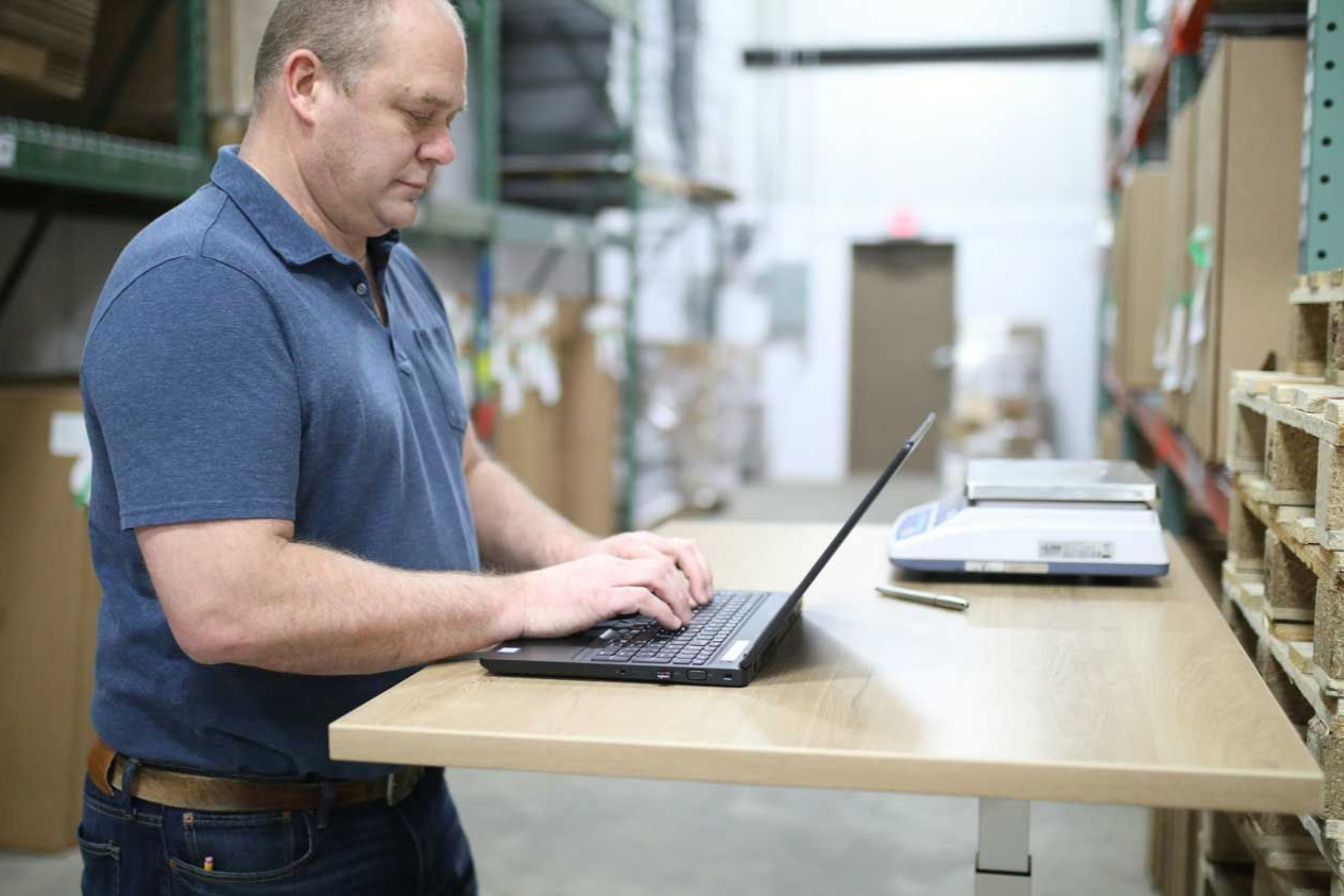 Man working on a laptop at a standing desk in a warehouse
