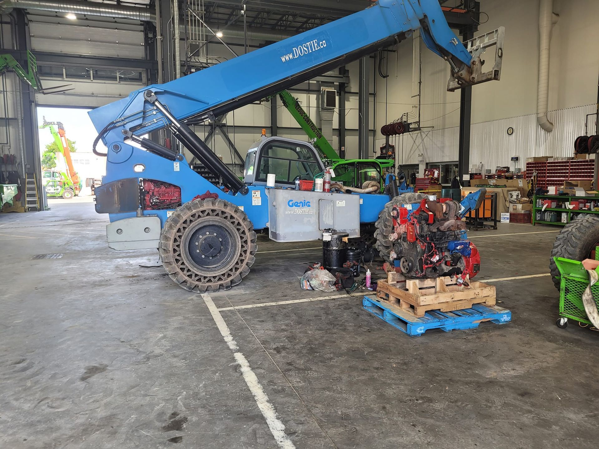 Chariot télescopique bleu dans un garage ; moteur sur une palette au premier plan.