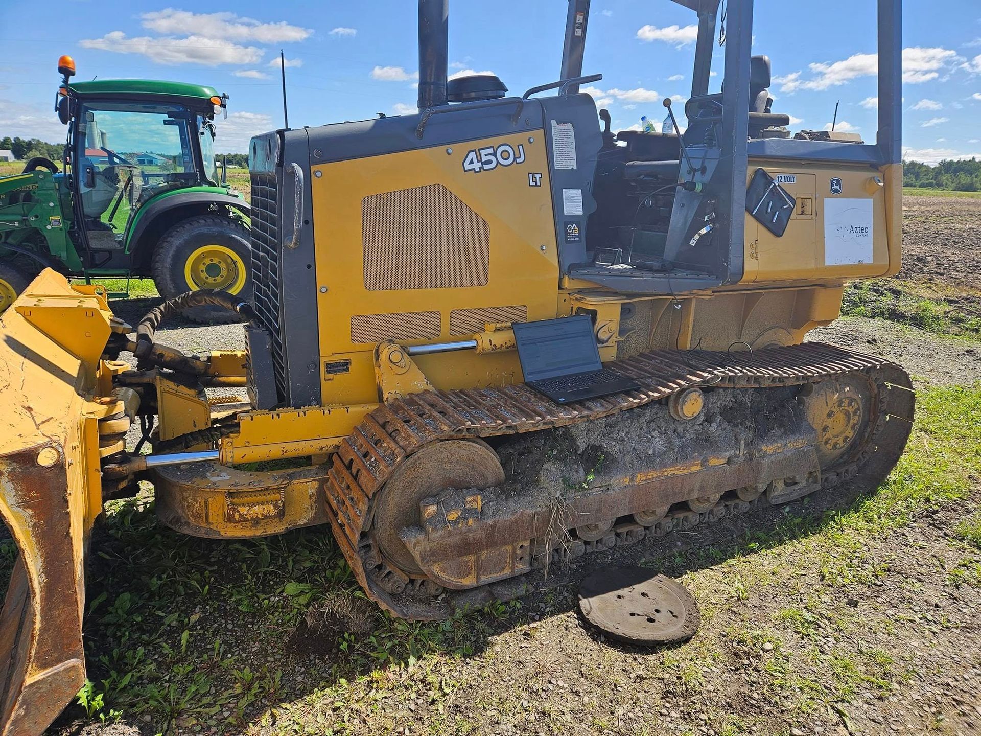 Bulldozer jaune à chenilles, stationné sur l'herbe à côté d'un tracteur John Deere.