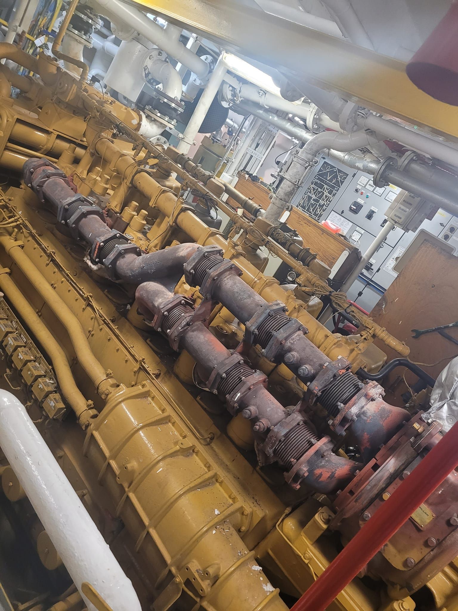 Moteur industriel jaune avec tuyaux rouillés et divers tubes dans un espace clos.