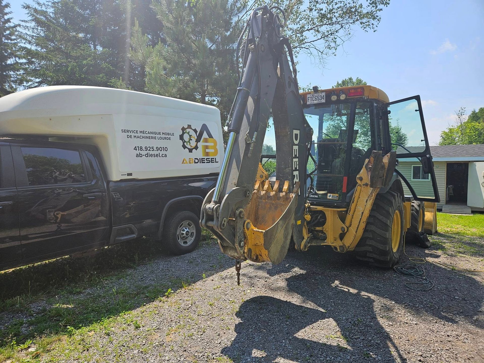 Camion noir avec capot blanc à côté d'une rétrocaveuse jaune, dans une cour de gravier.