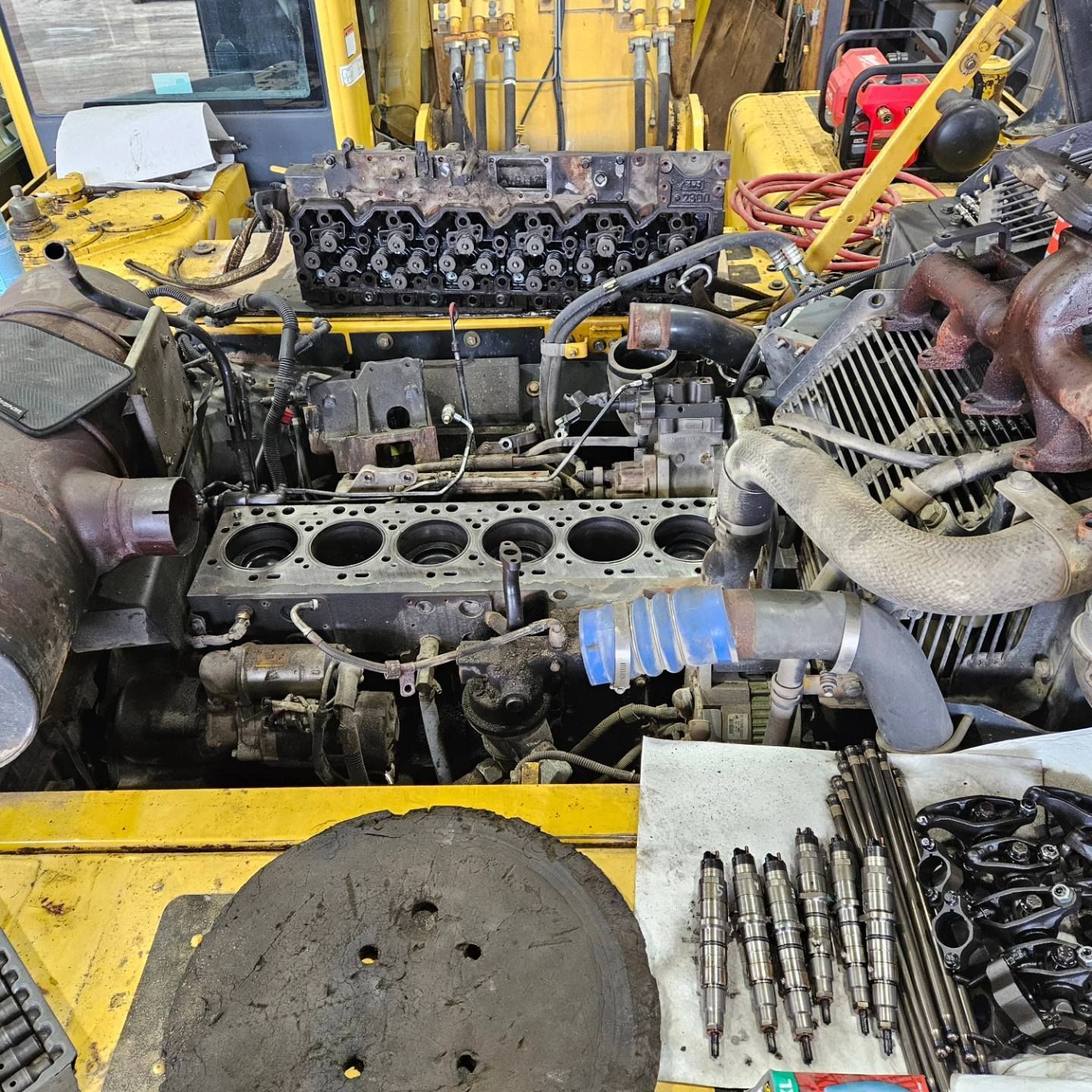 Un moteur diesel démonté sur une machine lourde jaune ; culasse, pièces et outils visibles.