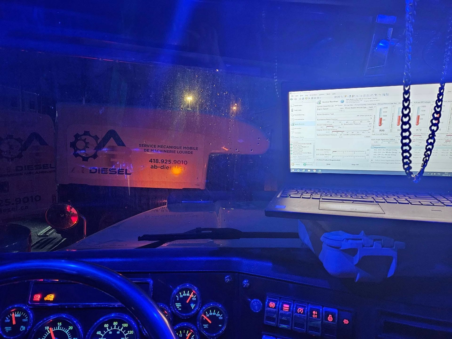À l'intérieur d'un véhicule la nuit, l'écran de l'ordinateur affiche du texte, des lumières bleues au néon, un volant et une bannière à l'extérieur.