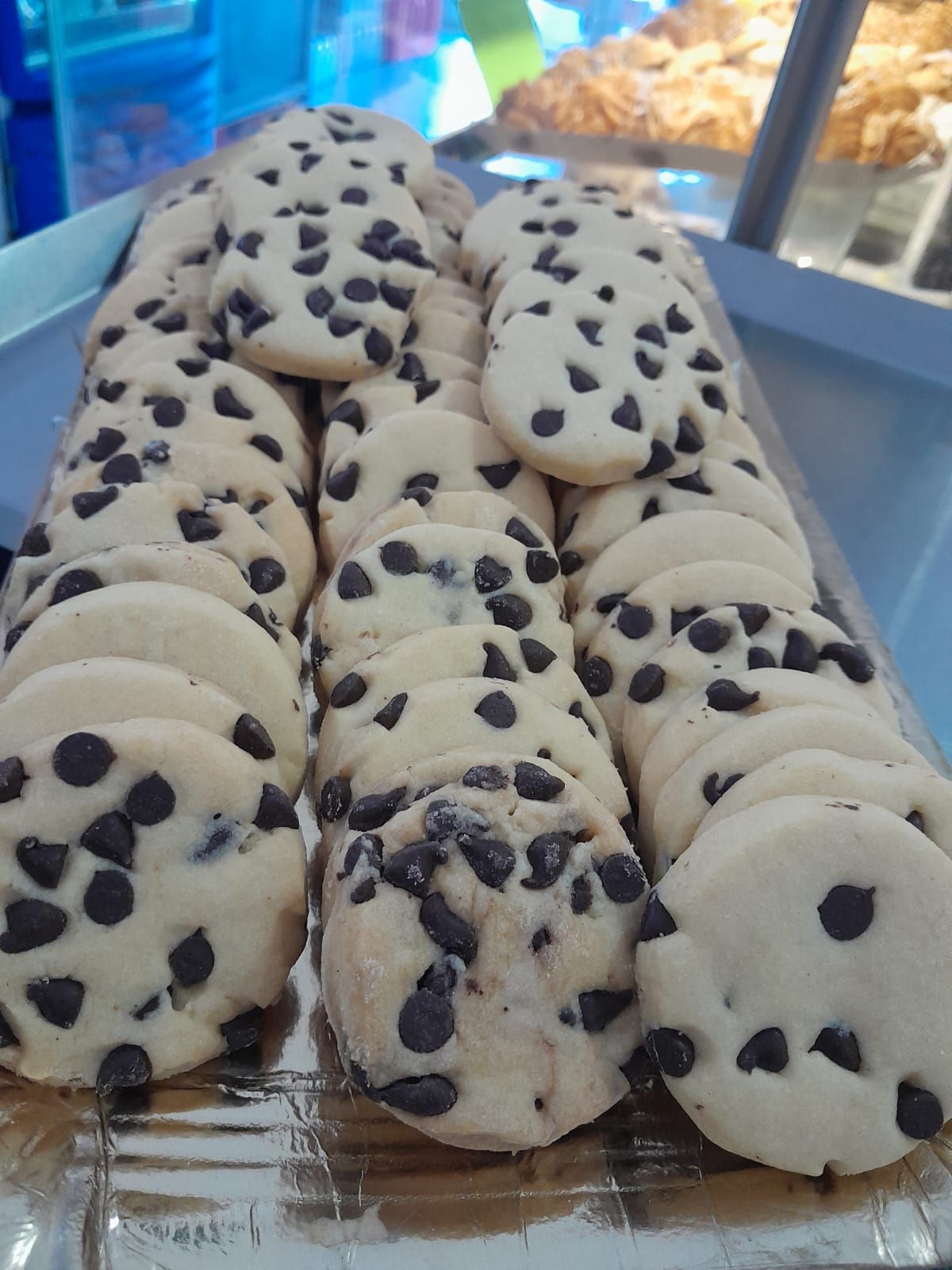 Filas de galletas con chispas de chocolate en una bandeja de plata, listas para exhibir.