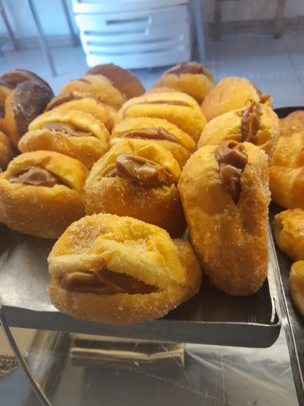 Bandeja de pasteles dorados rellenos de caramelo, espolvoreados con azúcar, exhibidos en un mostrador.