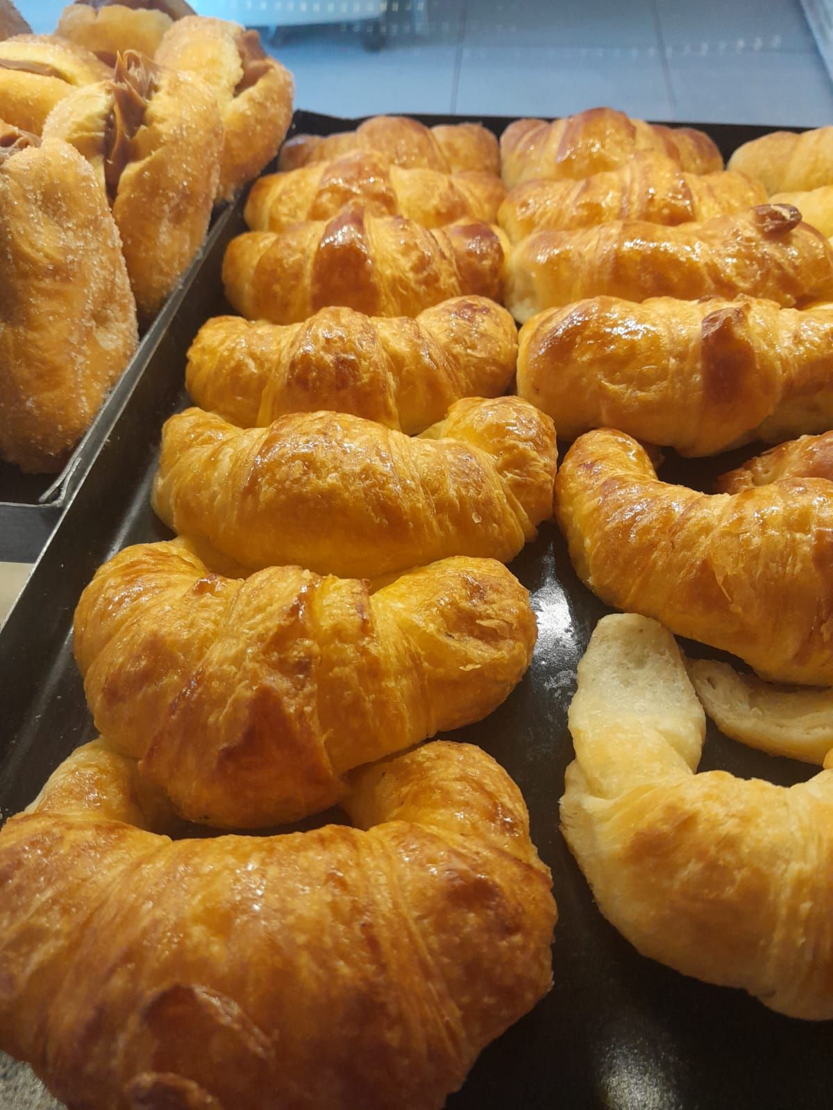 Primer plano de croissants dorados exhibidos en una bandeja negra en una panadería.