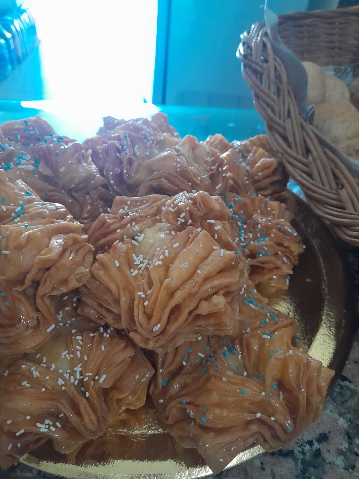 Pasteles fritos dorados con chispas azules en un plato dorado, junto a una canasta de mimbre.