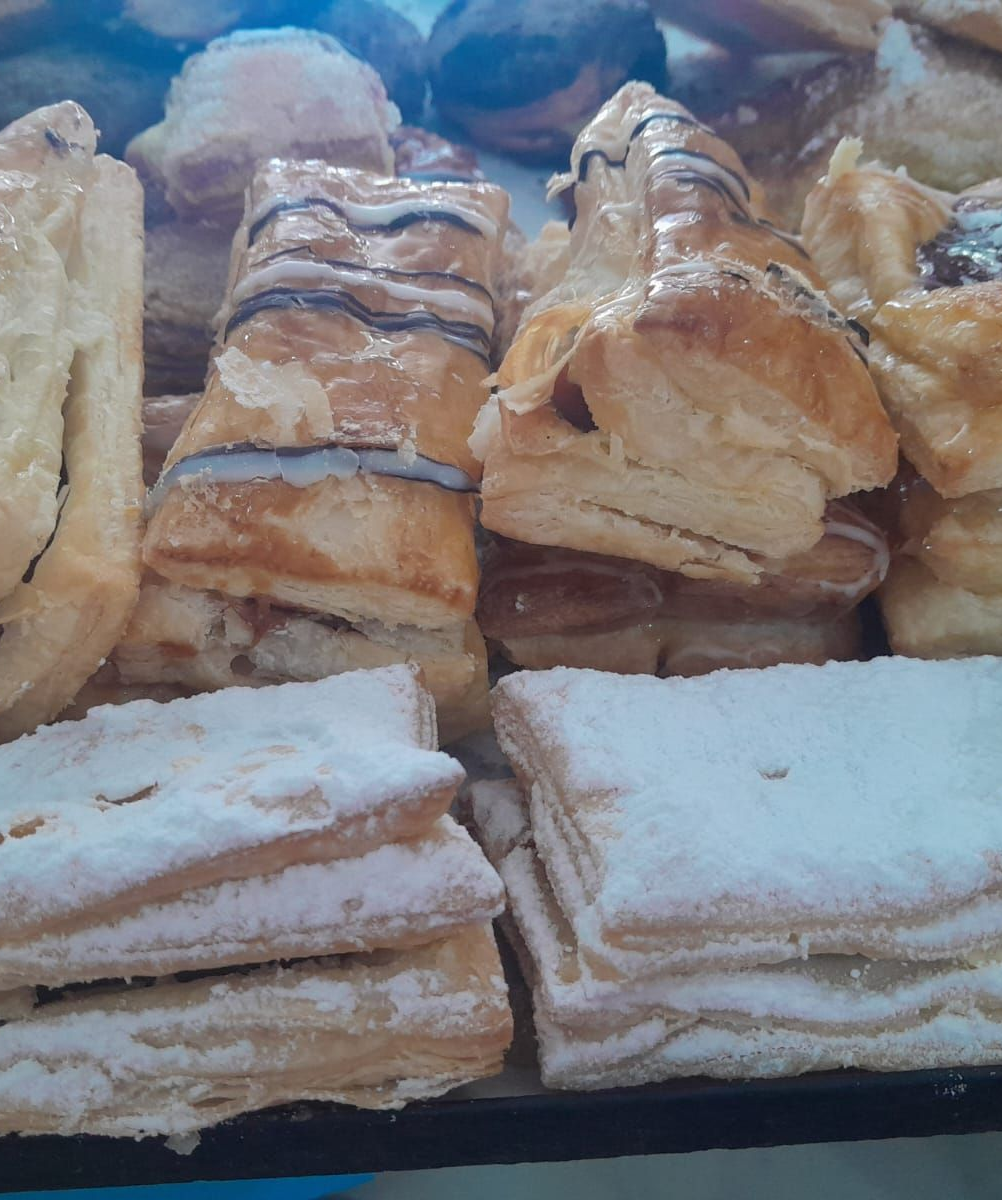Pasteles en exposición, algunos con chocolate o azúcar en polvo, en una vitrina de panadería.