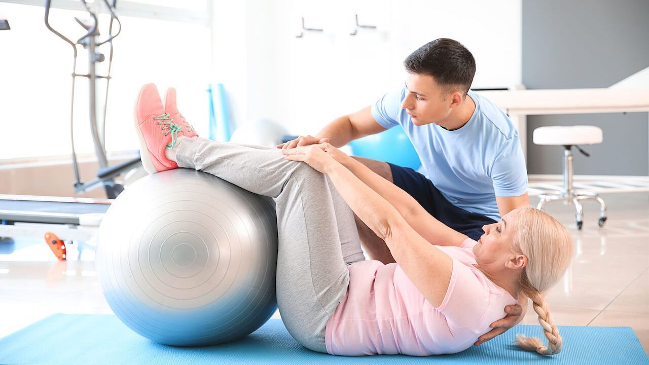 A physiotherapist is helping a woman do exercises on a pilates ball.