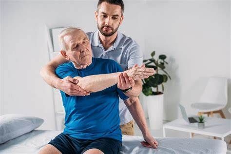 Chiropractor is helping an older man stretch his arm on a bed.