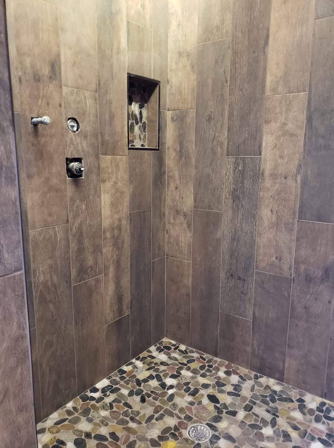 A shower with a stone floor and wooden walls.