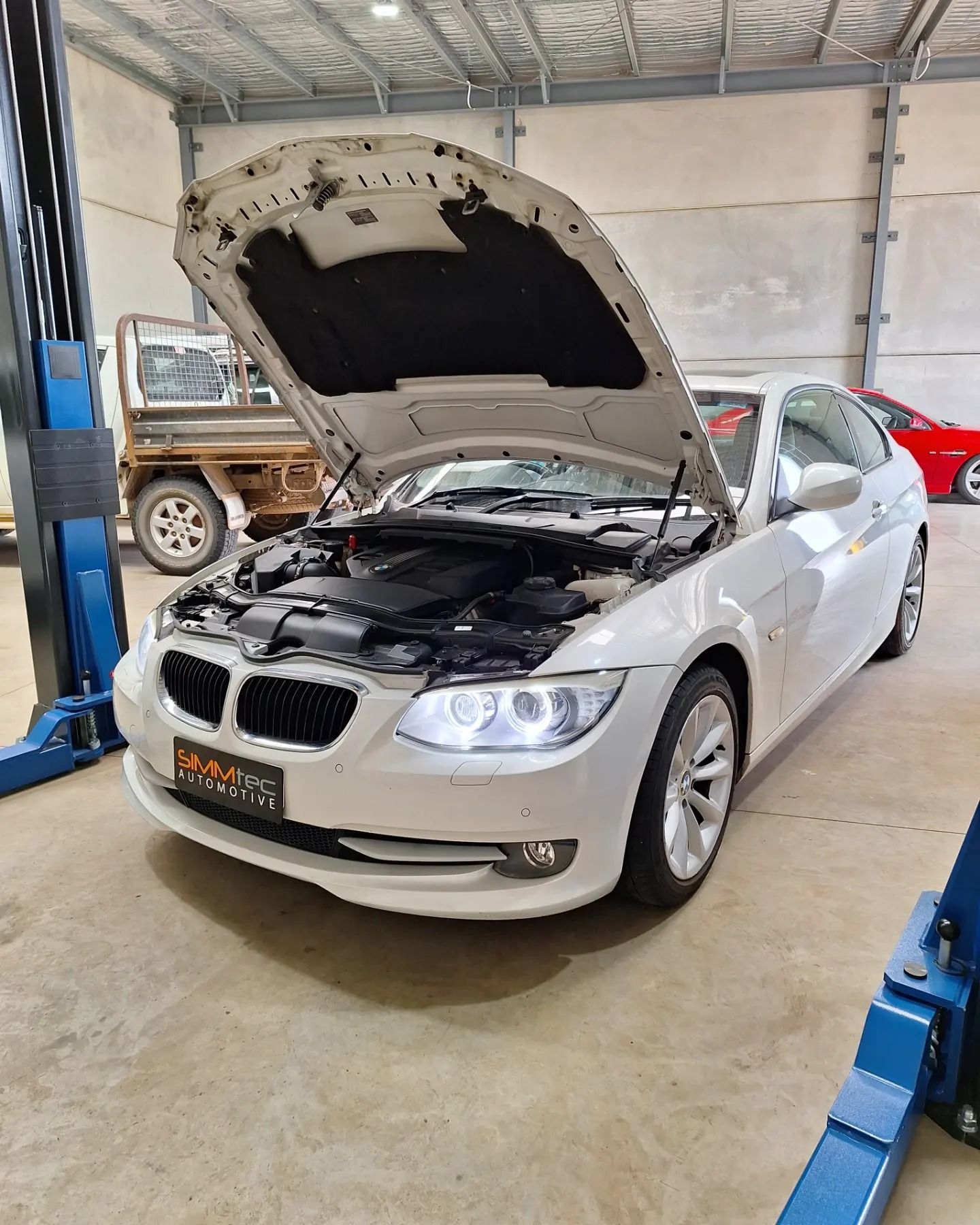 A white bmw is parked in a garage with the hood up.