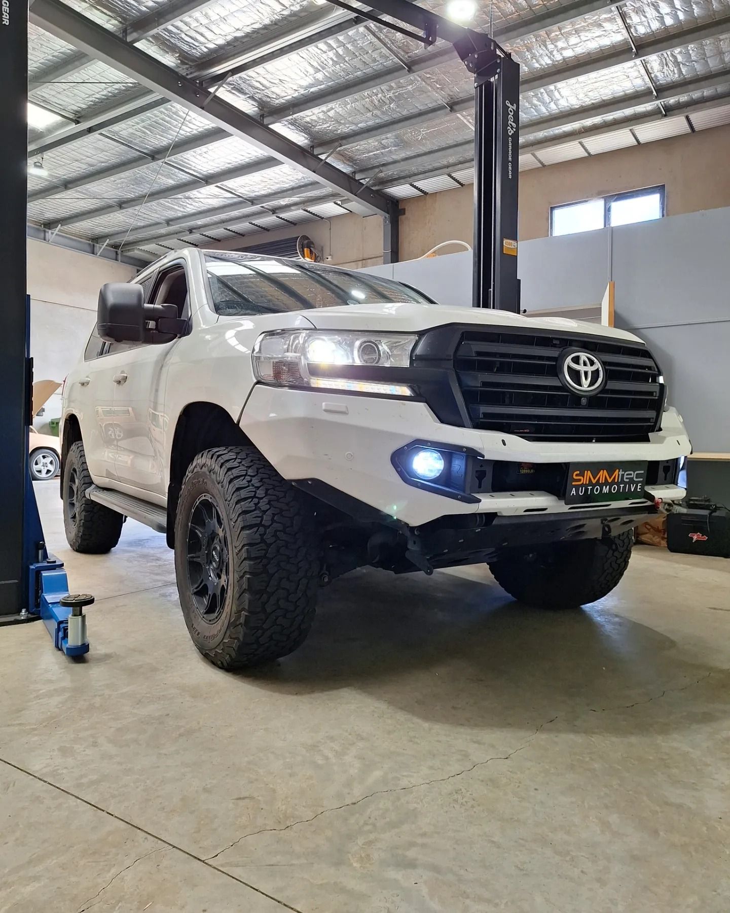 A white toyota land cruiser is parked in a garage on a lift.