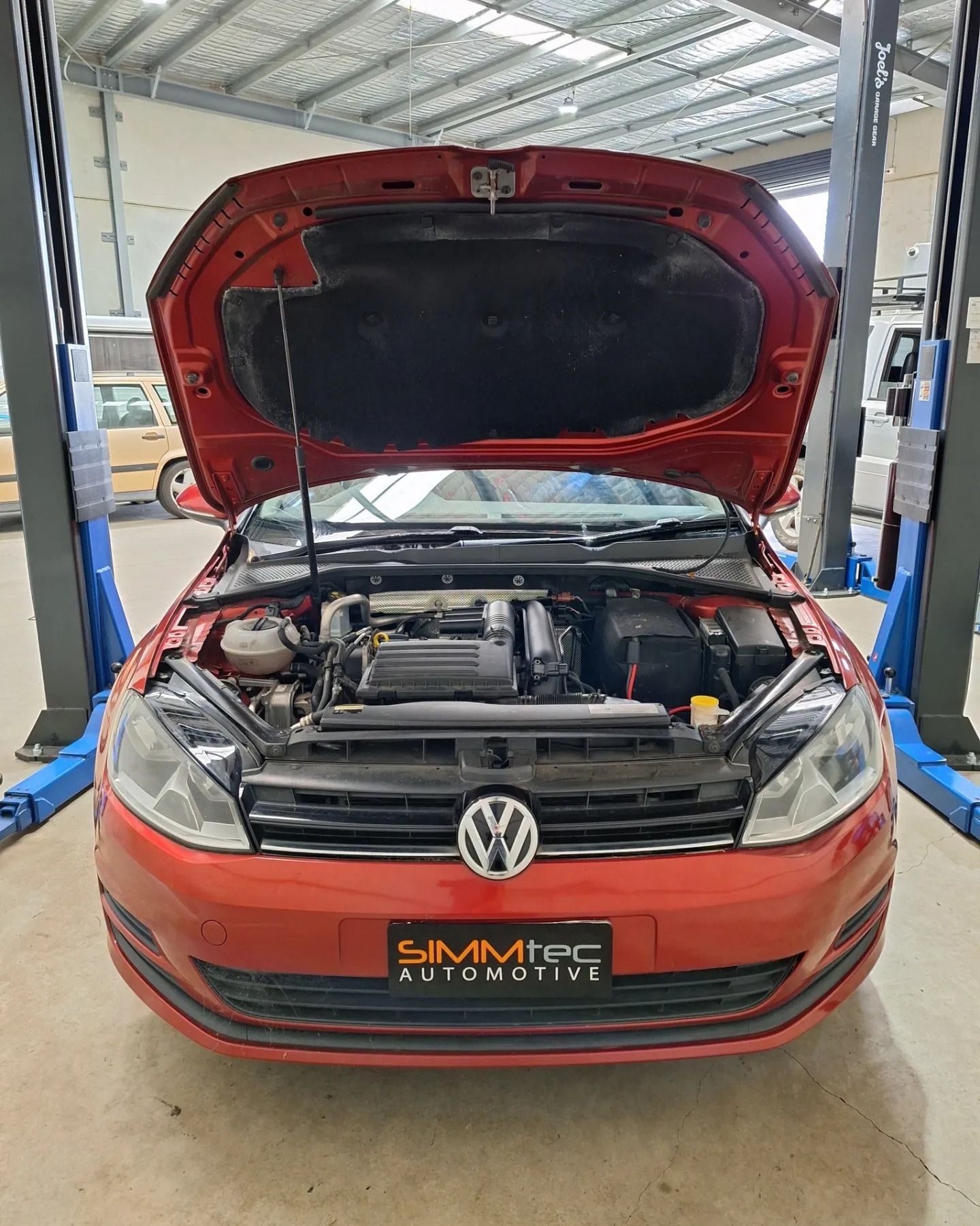 The hood of a red volkswagen golf is open in a garage.