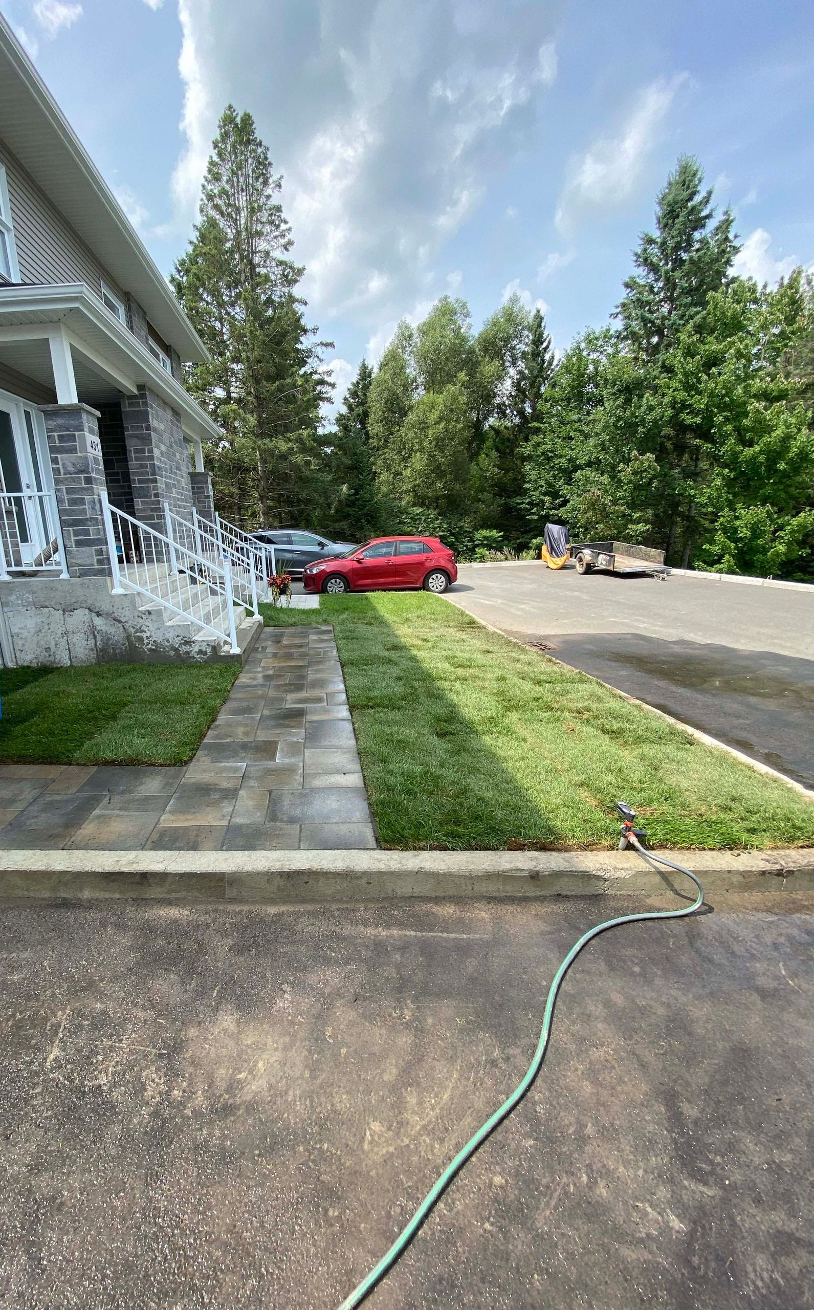 Une voiture rouge est garée devant une maison à côté d'un tuyau.