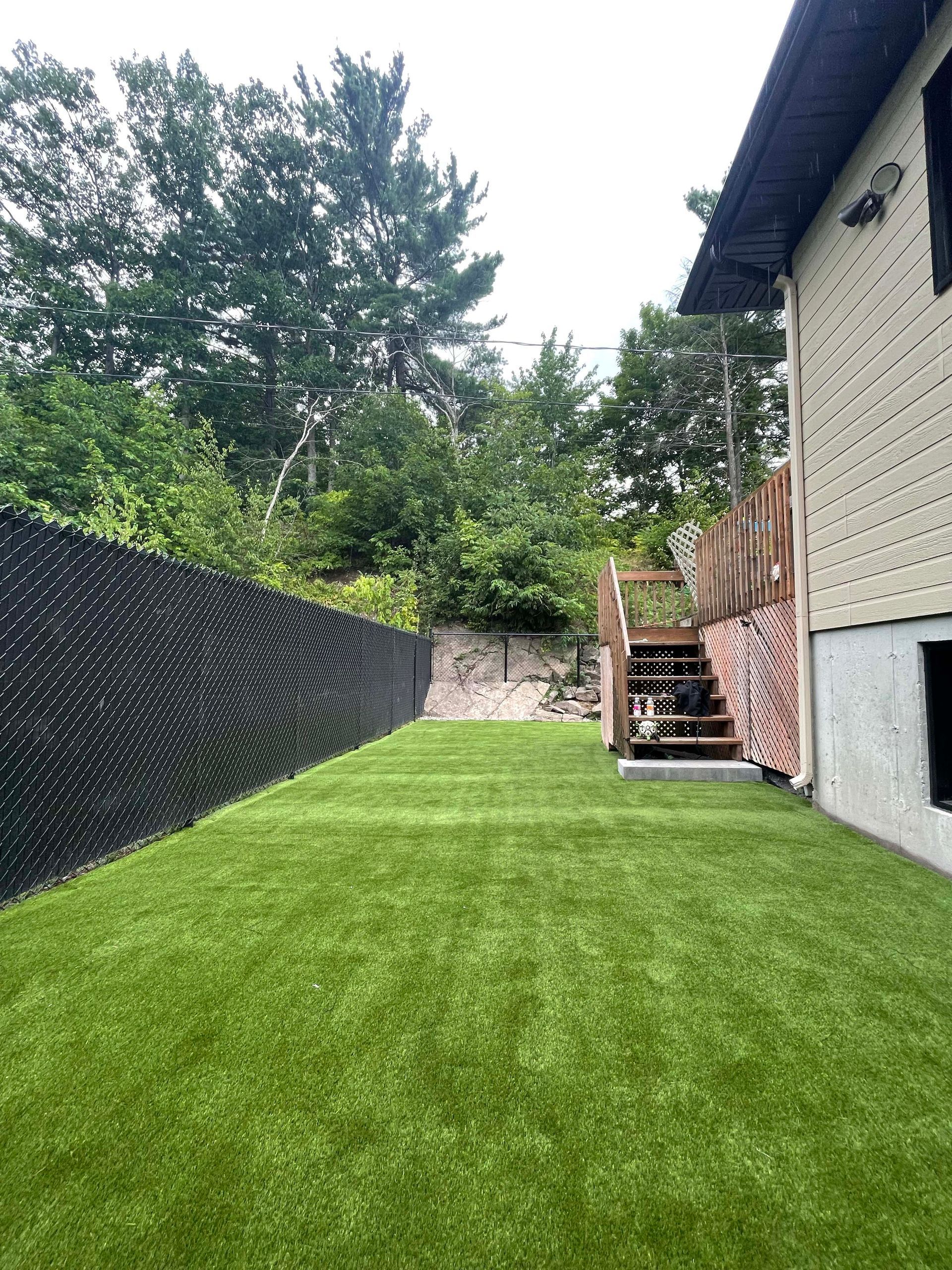 Une cour arrière avec une pelouse verte luxuriante et des escaliers menant à une terrasse.