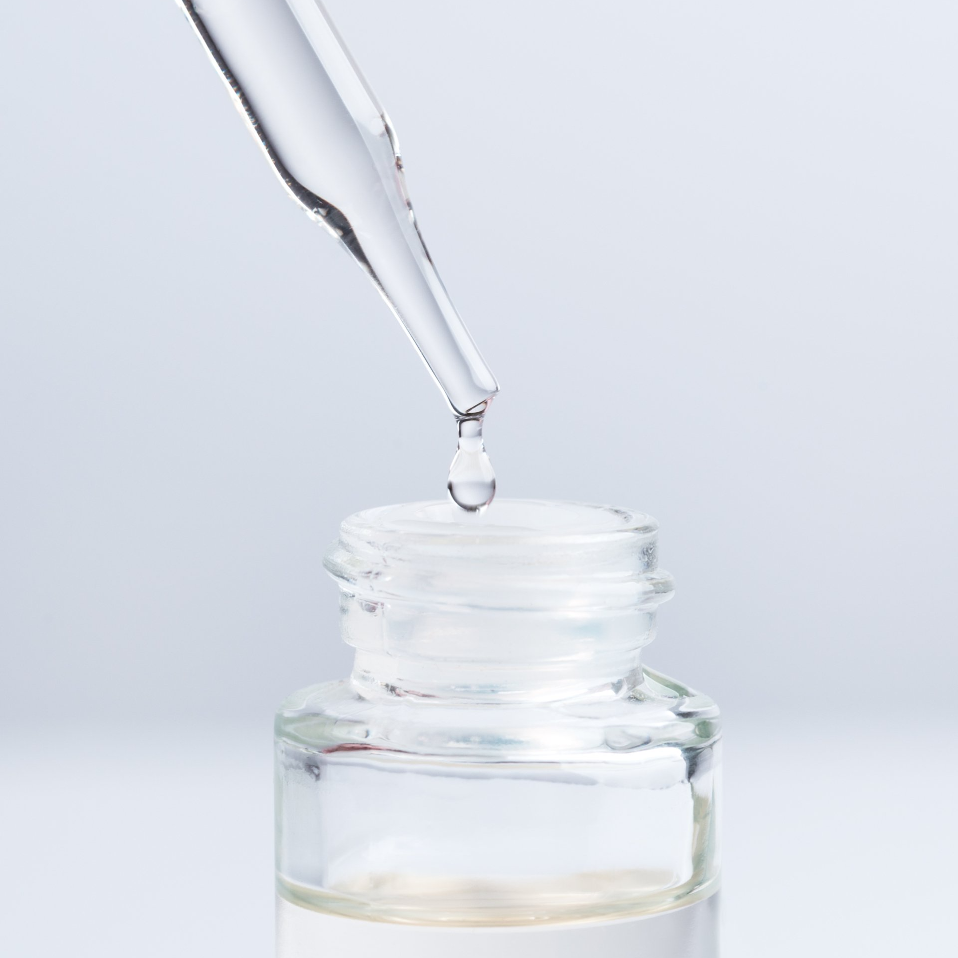 Dropping serum or collagen from a pipette. A pipette adding a drop of fluid or cosmetic oil to vial on a light background. Medicine or beauty industry concept.
