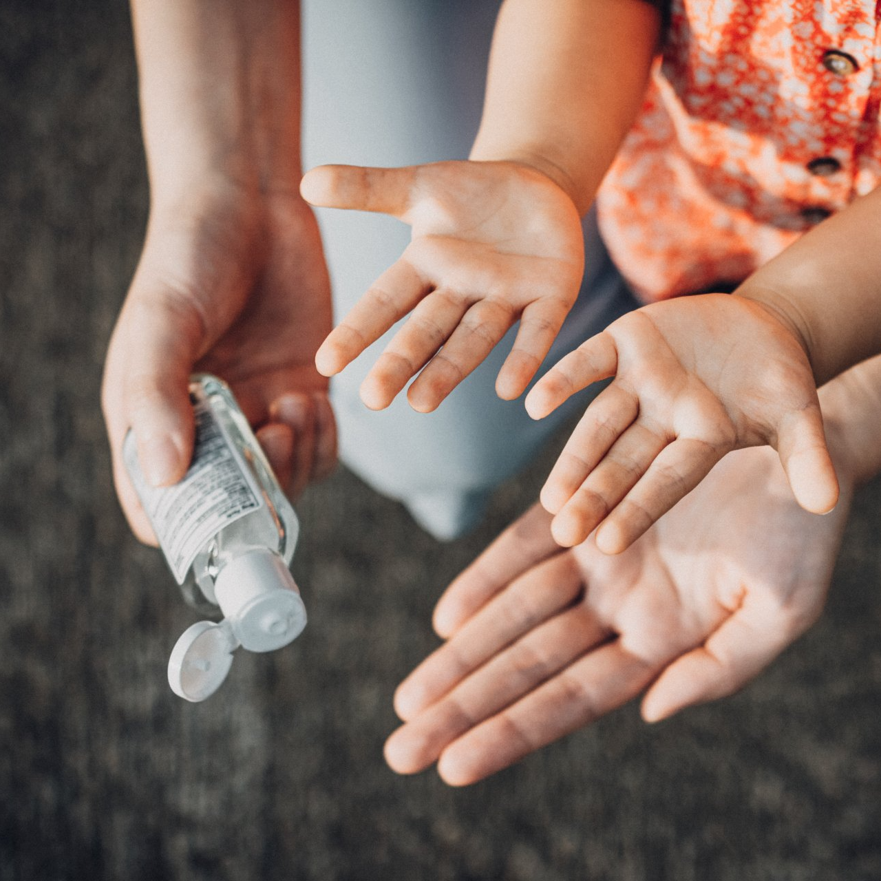 Mother squeezing hand sanitizer onto little daughter's hand outdoors to prevent the spread of viruses