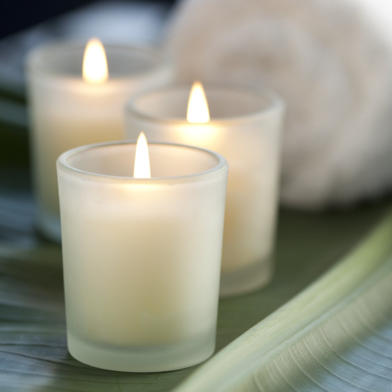 Three candles in spa setting, with banana leaf and white towels