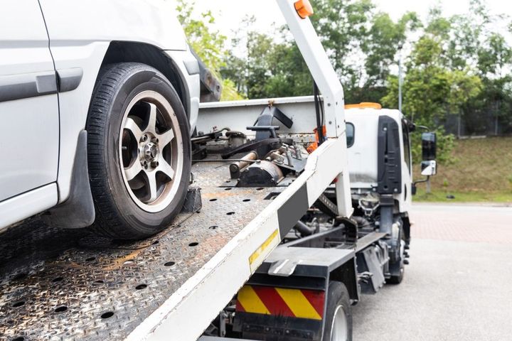 White car being towed on a tow truck, on a road.