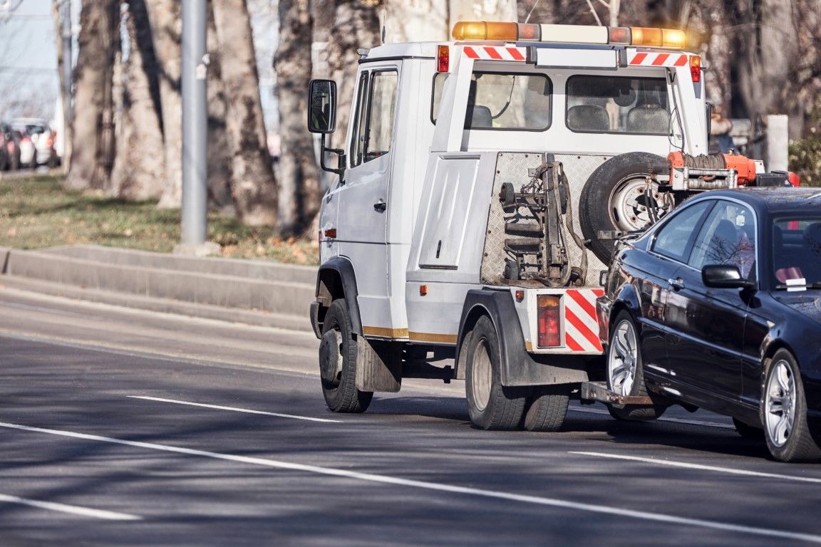 Tow truck towing a black car on a city street.