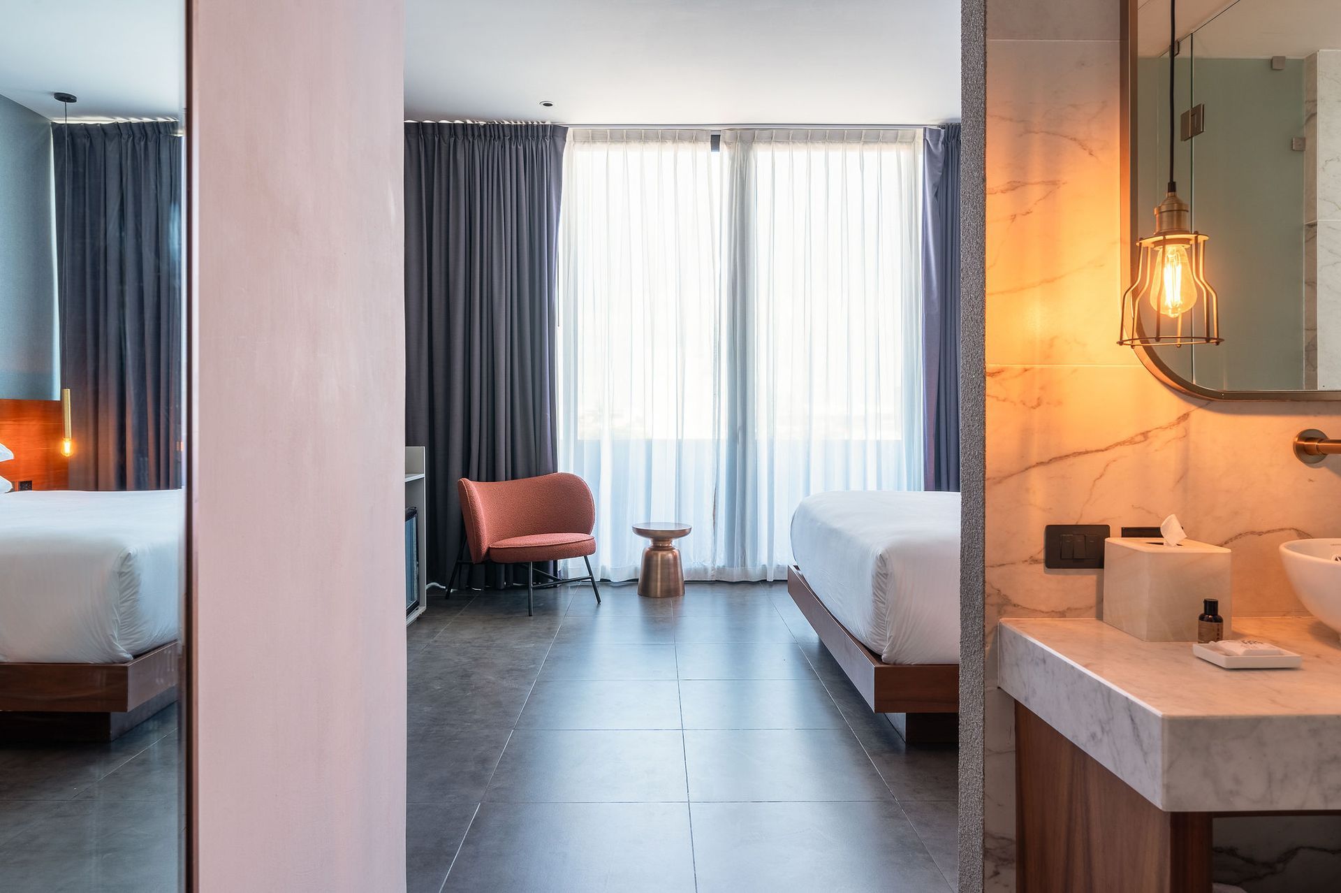 A hotel room with a bed , chair , sink and mirror.