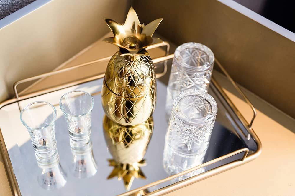 A pineapple shaped ice bucket and shot glasses on a tray.