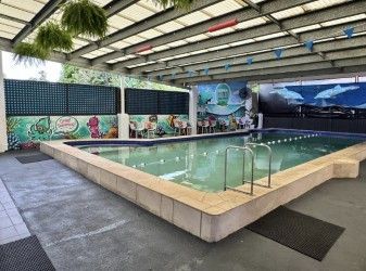 Indoor swimming pool with a raised square basin, tile deck, and mural-covered walls
