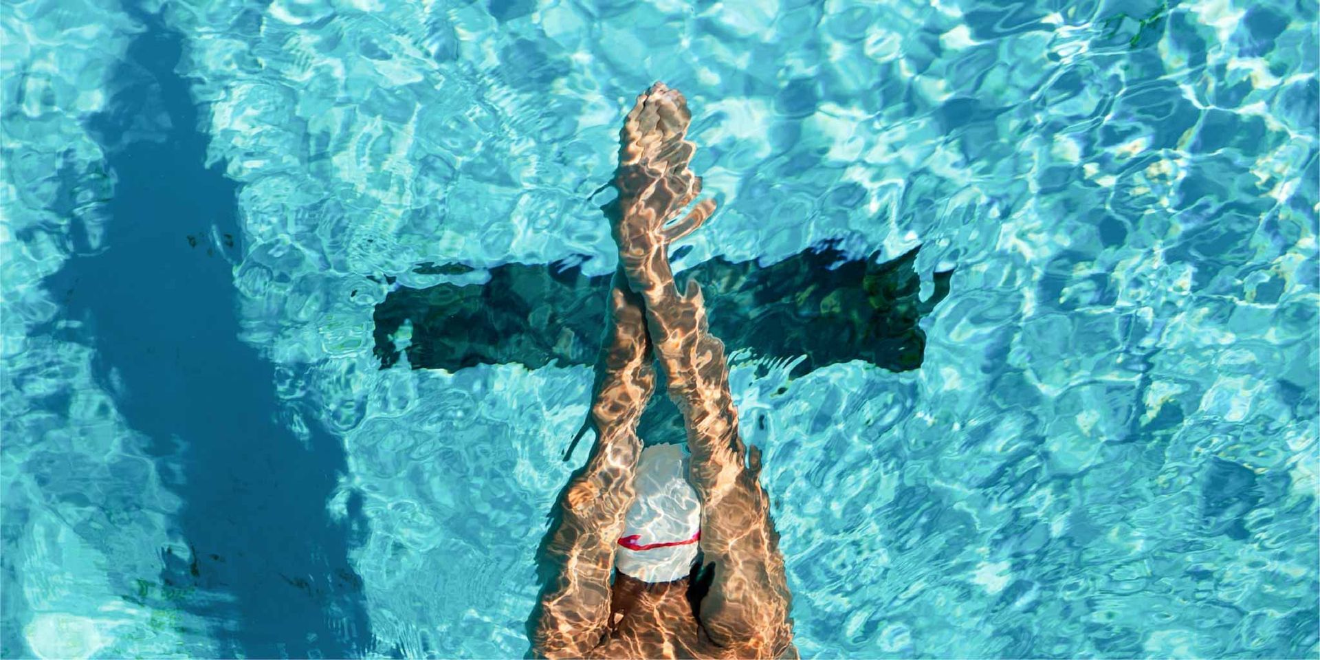 Swimmer floating on back in a blue pool, arms extended overhead