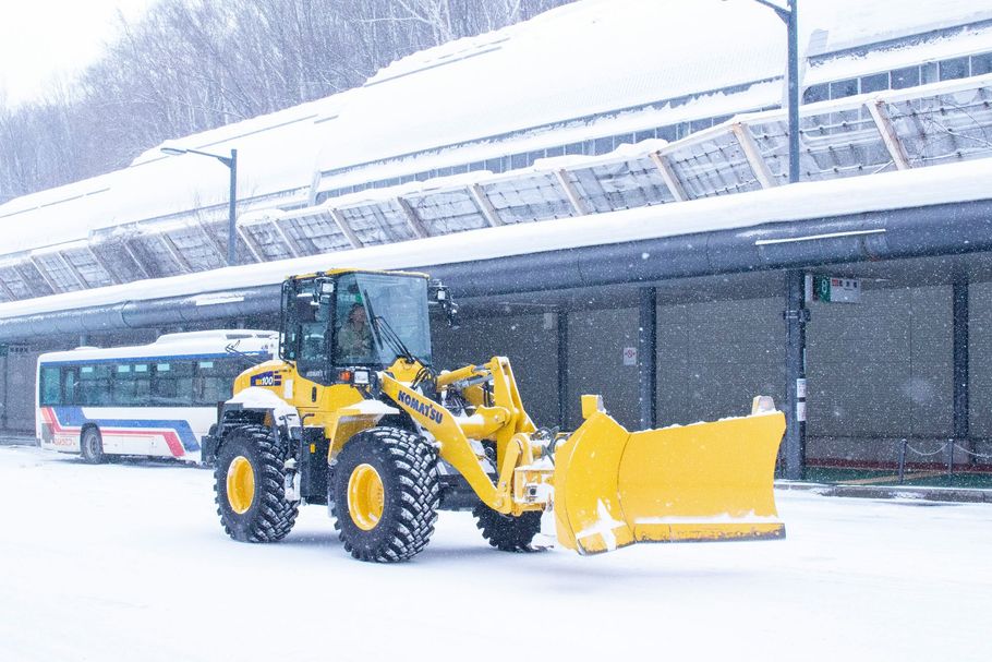 Yellow snowplow clearing snow outside a bus station in a heavy snowfall