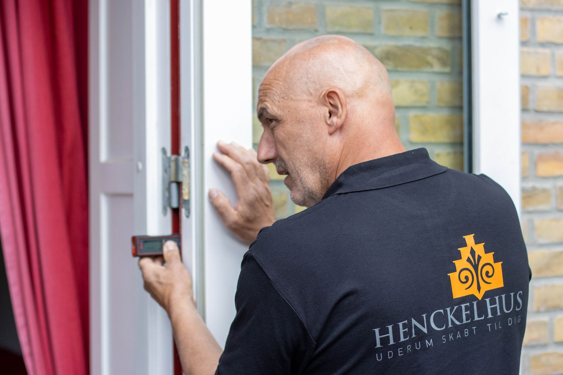 En mand i sort skjorte med ordet henckelhus på ryggen åbner en dør.